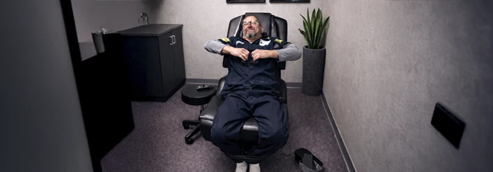 A technician relaxes in a recliner during a workplace wellness session in a private, minimalist room.